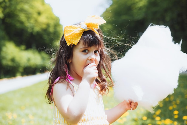 Una bambina con un vestito giallo durante una passeggiata in un parco di divertimenti mangia zucchero filato