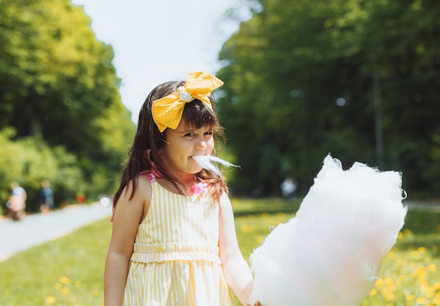 Una bambina con un vestito giallo durante una passeggiata in un parco di divertimenti mangia zucchero filato