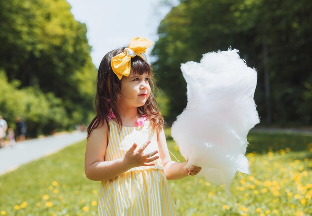 Una bambina con un vestito giallo durante una passeggiata in un parco di divertimenti mangia zucchero filato