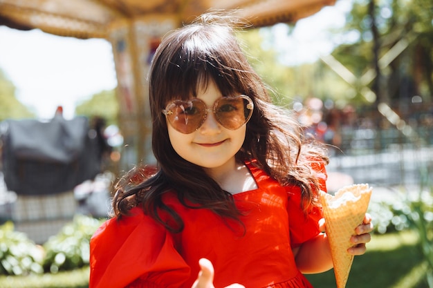 Una bambina con un vestito rosso e un cappello di paglia mangia il gelato in un cono nel parco