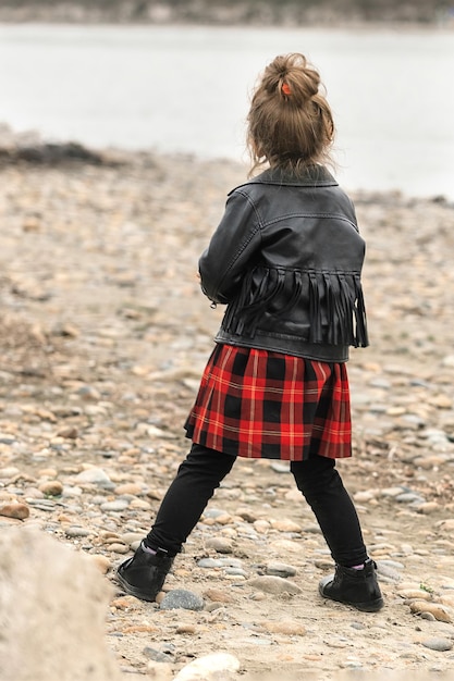 una bambina con un vestito scozzese rosso acceso e una giacca di pelle si diverte durante una passeggiata lungo il fiume