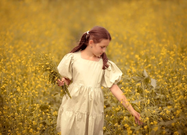 una bambina con un vestito si trova in un campo con fiori gialli e raccoglie fiori in un bouquet