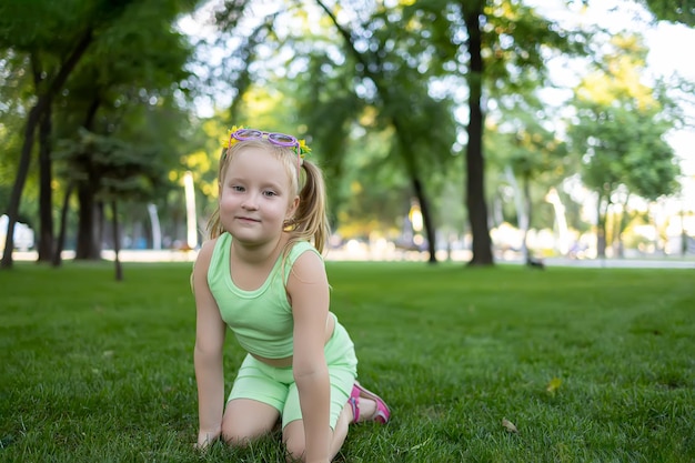 Una bambina con un vestito verde si siede sul prato del parco e posa per la macchina fotografica