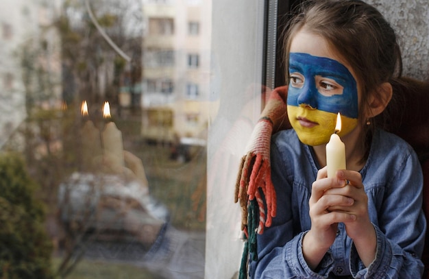 Una bambina con una bandiera ucraina dipinta sul viso che prega con una candela in mano per la città ucraina di Bucha è un gesto di fede e di speranza Bambini contro la guerra