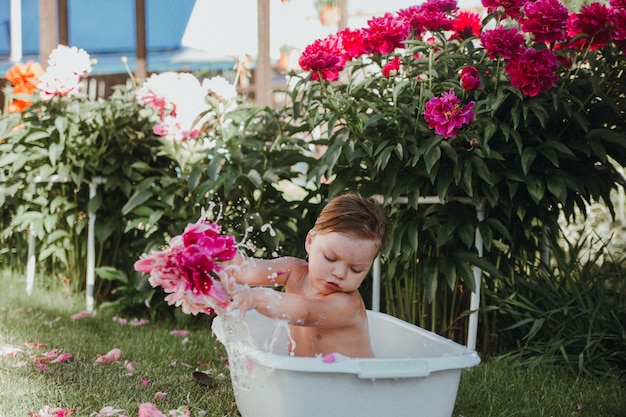 Una bambina con una corona in testa sta facendo il bagno in una piccola vasca con peonie