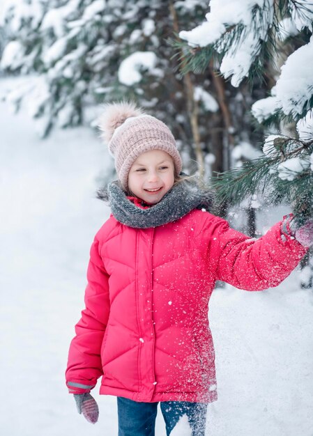 Una bambina con una giacca luminosa gioca nella foresta innevata d'inverno.