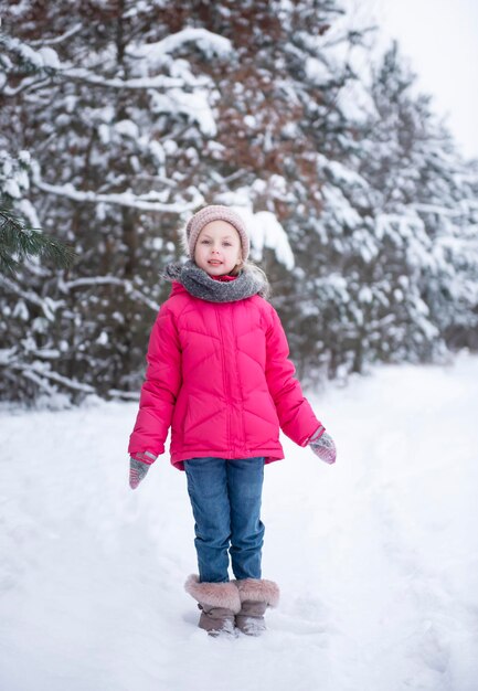 Una bambina con una giacca luminosa gioca nella foresta innevata d'inverno.