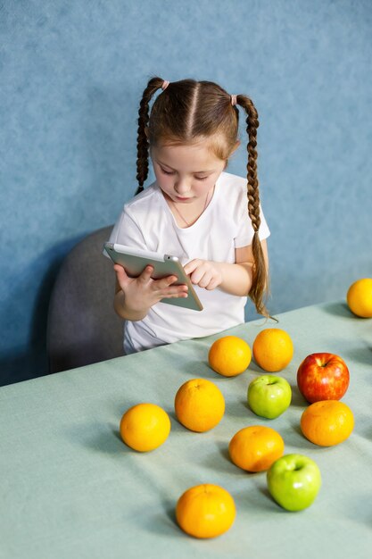 Una bambina con una maglietta bianca tiene in mano un tablet e studia i frutti