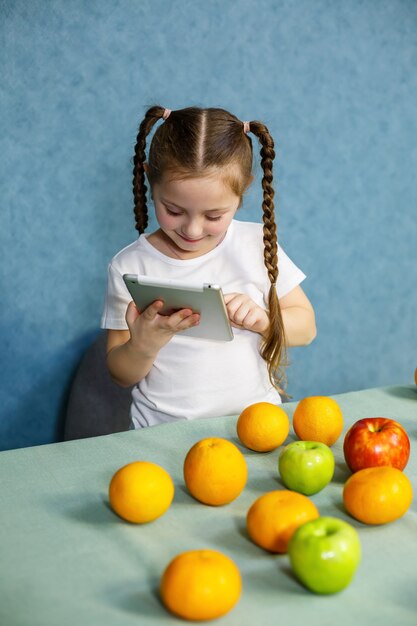 Una bambina con una maglietta bianca tiene in mano un tablet e studia i frutti