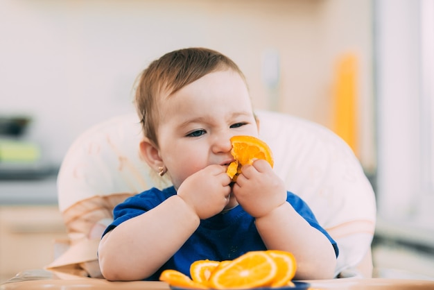 una bambina con una maglietta blu e un piatto blu seduto sulla sedia di un bambino che mangia un'arancia