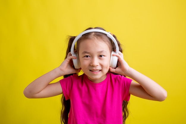 Una bambina con una maglietta rosa con le cuffie per ascoltare musica su sfondo giallo