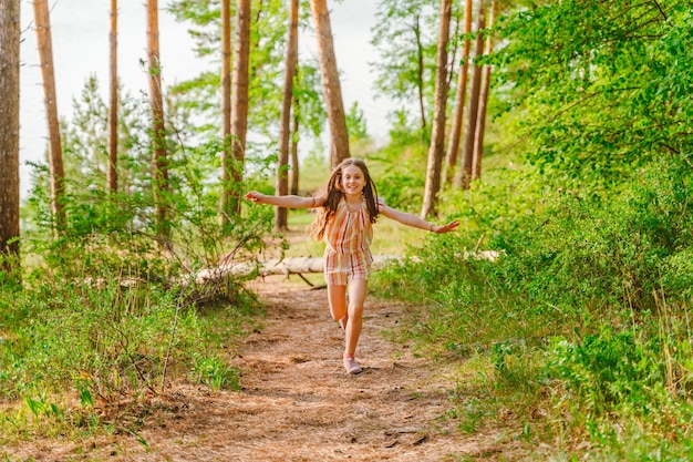 Una bambina corre felice con le braccia aperte su un sentiero nella foresta