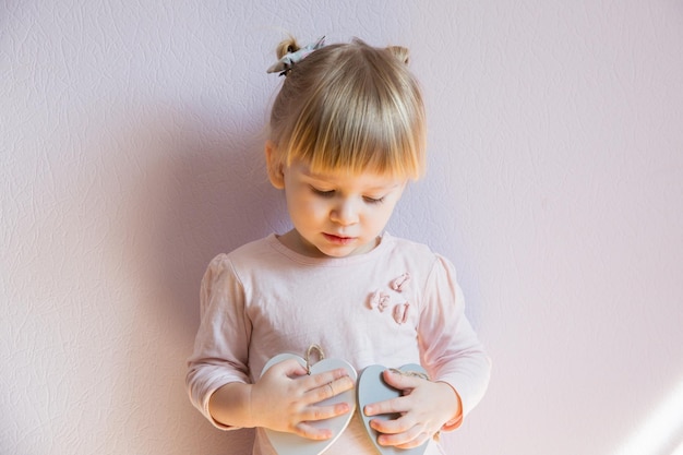 Una bambina dai capelli biondi tiene in mano due cuori bianchi di legno