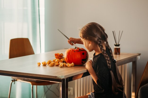 Una bambina decora una zucca in una stanza per Halloween. I bambini decorano la casa. I bambini intagliano la zucca. Divertimento spettrale di Halloween