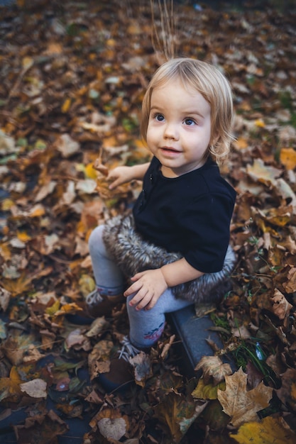 Una bambina di 1,5 anni è in piedi e sorride. Il bambino lancia le foglie. Ragazza allegra nella foresta autunnale