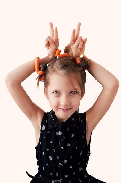 Una bambina di 6 anni con i bigodini in testa che scherzano alla ricerca della bellezzaLe gioie dei bambini isolati su sfondo bianco