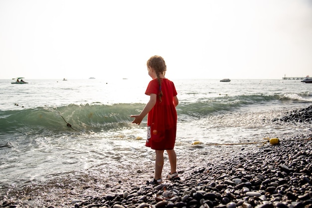 Una bambina di 6 anni sul mare salta sulle onde e si diverte. Vacanze di famiglia. Infanzia. Estate.