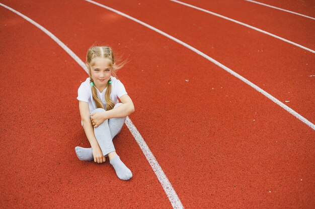 Una bambina di 78 anni con una maglietta bianca corre all'aperto nello stadio La ragazza sta facendo sport in una giornata di sole