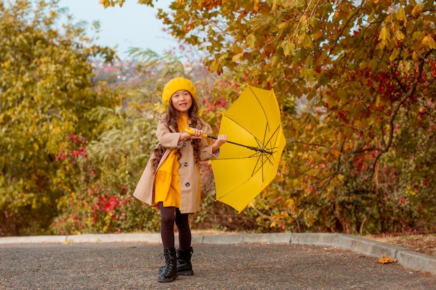 Una bambina di aspetto asiatico tiene un ombrello giallo in autunno