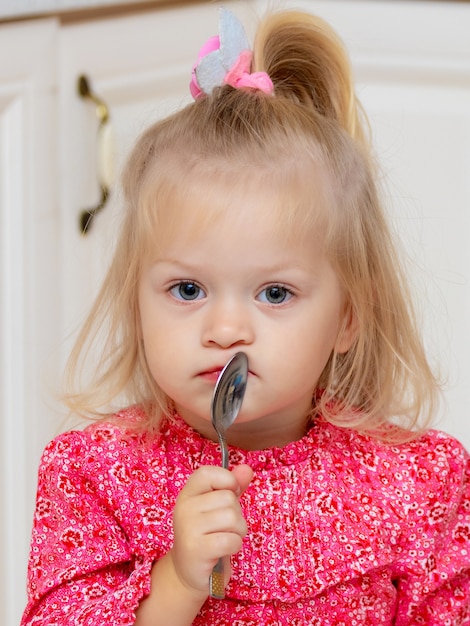 Una bambina di due anni con un cucchiaio vicino alla bocca e un'espressione pensierosa sul viso