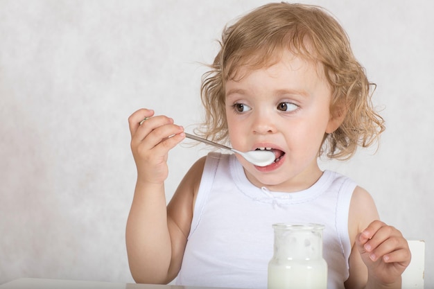 Una bambina di due anni sta mangiando yogurt naturale senza zucchero. Avvicinamento