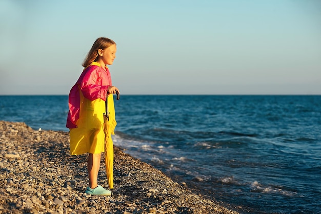 Una bambina di otto anni in abiti autunnali sulla riva del mare blu