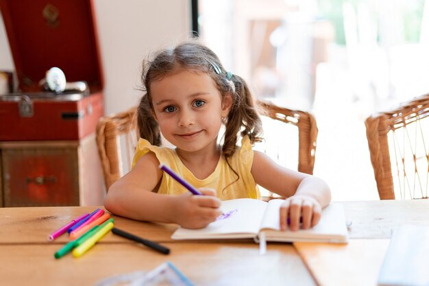 Una bambina di prima elementare disegna su un quaderno usando un pennarello viola, riposando dopo la scuola mentre è seduta a un tavolo di legno di casa.