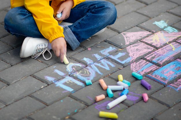 Una bambina di sei anni disegna una casa sull'asfalto con i pastelli. È primavera e fa caldo fuori. Il concetto di intimità. Tutti hanno bisogno di una casa. Infanzia. Strada.