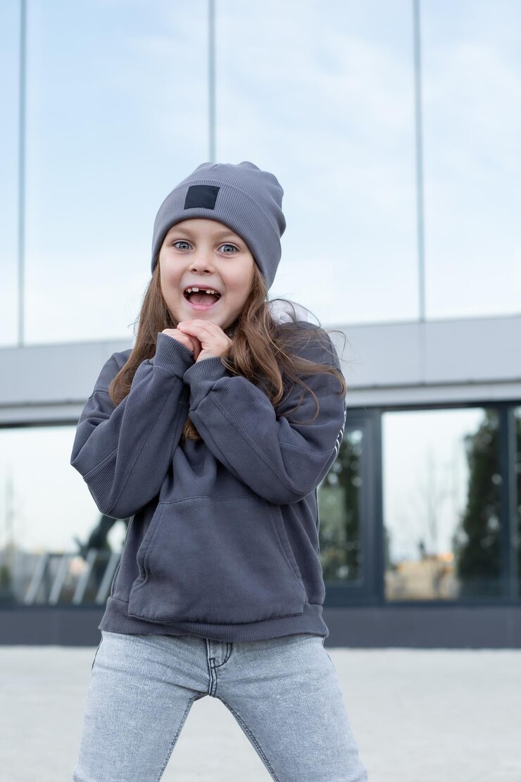 una bambina di sei anni in jeans e una felpa con cappuccio grigia balla hiphop sullo sfondo di uno specchio