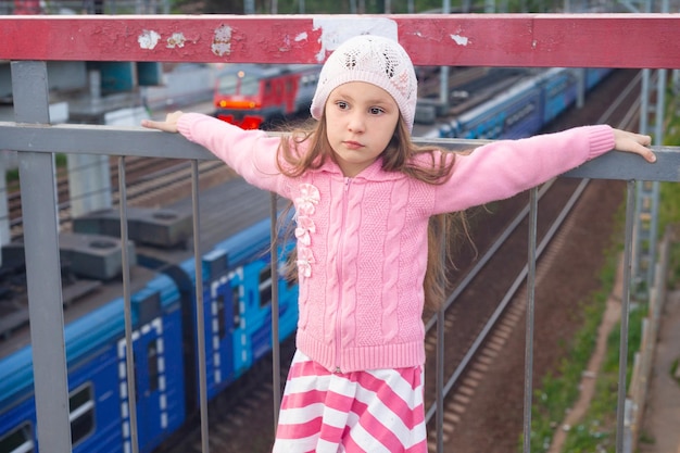 Una bambina di sei anni vestita di rosa sta su un ponte sopra i binari della ferrovia