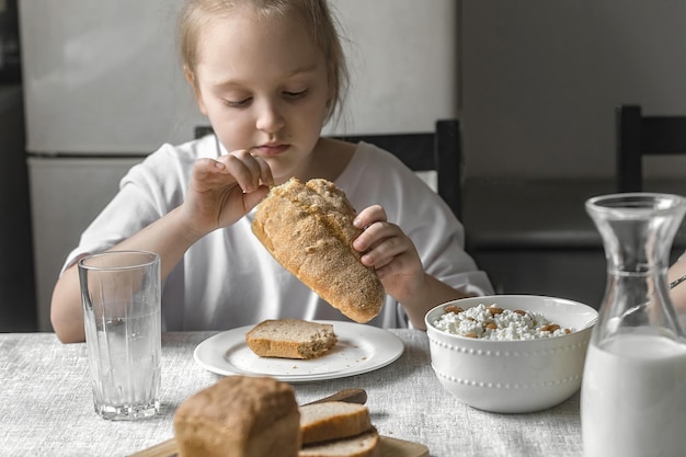 una bambina di sette anni durante la colazione a casa in cucina prova una pagnotta spezzata