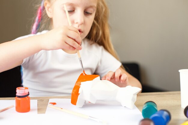 Una bambina dipinge una volpe giocattolo fatta di argilla concetto fai-da-te