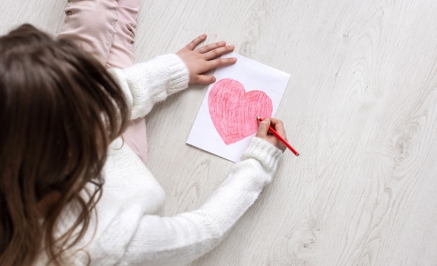 Una bambina disegna un cuore sul pavimento