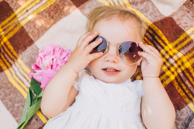 Una bambina è sdraiata su un copriletto a scacchi e sta provando con gli occhiali da sole.