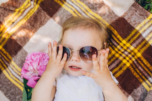 Una bambina è sdraiata su un copriletto a scacchi e sta provando con gli occhiali da sole.