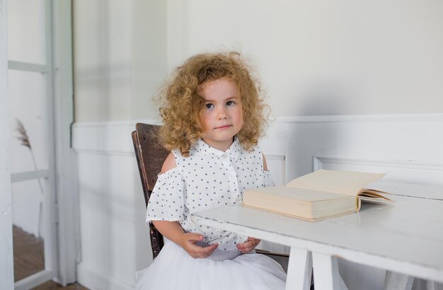 Una bambina è seduta a un tavolo davanti a un libro aperto. scuola a casa