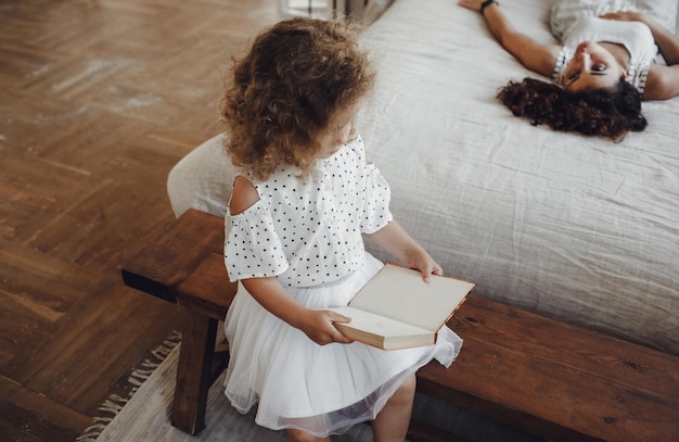 Una bambina è seduta con un libro in mano accanto a sua madre. leggere libri per bambini