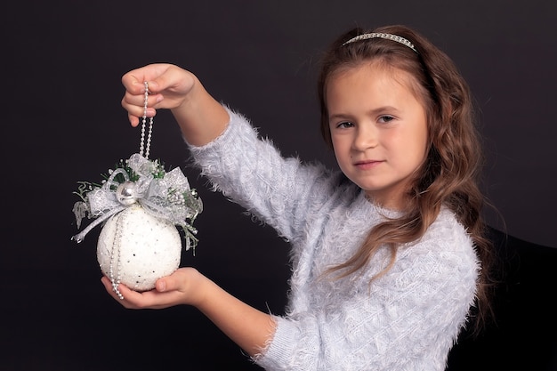 Una bambina è seduta in un bellissimo vestito e tiene in mano una pallina di Natale