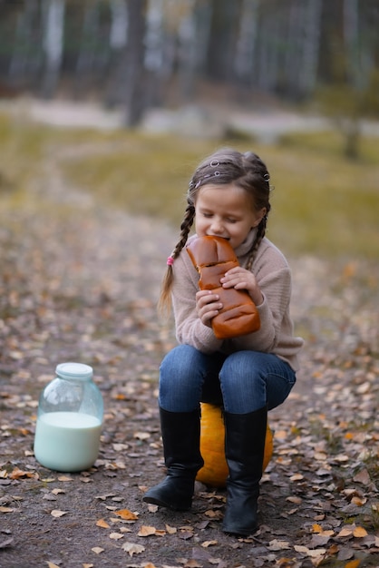 Una bambina è seduta su una zucca, mangia il pane, accanto a un barattolo di latte