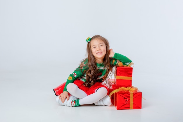 Una bambina è seduta su uno sfondo bianco con regali di Natale in isolamento