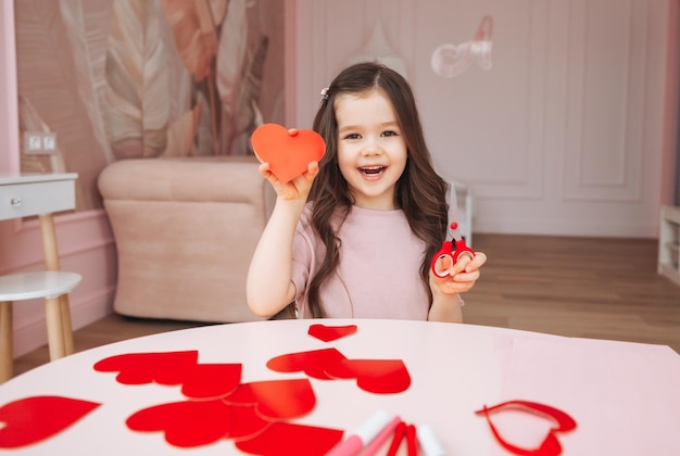 Una bambina fa le carte di San Valentino usando forbici di carta colorata e matita seduta a un tavolo