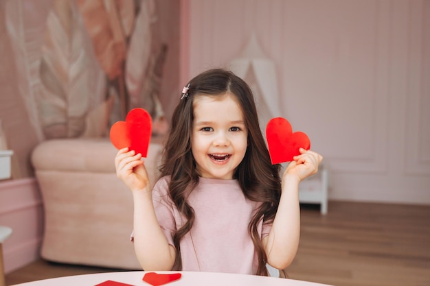 Una bambina fa le carte di San Valentino usando forbici di carta colorata e matita seduta a un tavolo