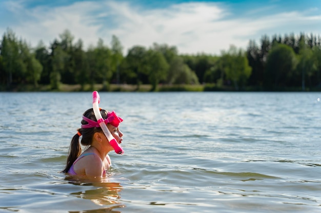 Una bambina fa snorkeling su un lago in una giornata estiva indossando una maschera rosa e un boccaglio subacqueo