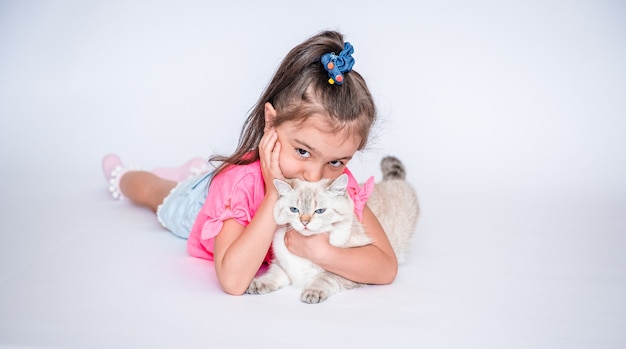 Una bambina felice abbraccia un gatto bianco di razza britannica sdraiato su uno sfondo bianco Pets Girl