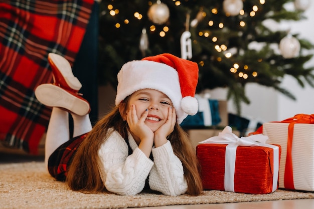 Una bambina felice con un cappello di Babbo Natale sorride con doni nelle sue mani.