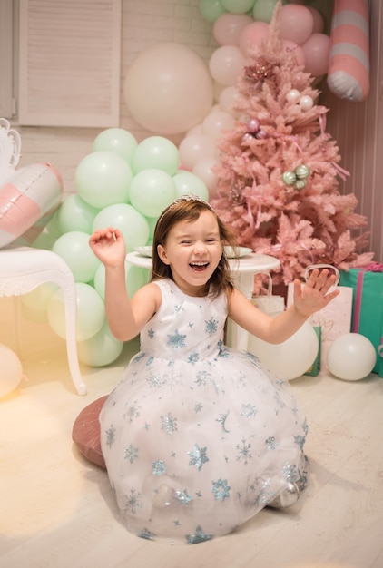 Una bambina felice con un vestito soffice è seduta sui cuscini nelle decorazioni del nuovo anno