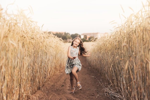 Una bambina felice corre attraverso un campo di grano in estate in una giornata di sole. Estate. Vacanze estive. Infanzia felice. Emozioni ed energia positive