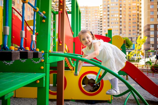 Una bambina felice gioca nel complesso parco giochi per bambini vicino alla casa in estate nel cortile e sorride