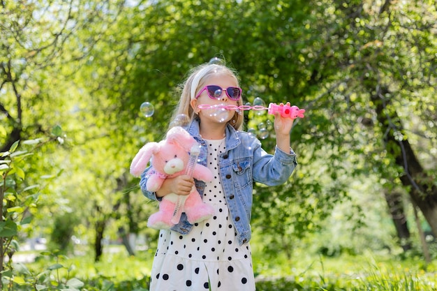 Una bambina felice in estate con gli occhiali da sole gonfia le bolle di sapone tiene un giocattolo nelle sue mani