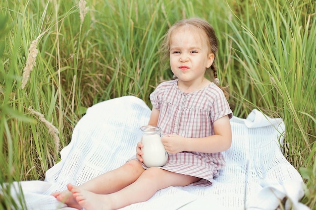 Una bambina felice in un campo di grano con pane e una brocca di latte fresco. Passeggiate estive nel villaggio. infanzia felice.